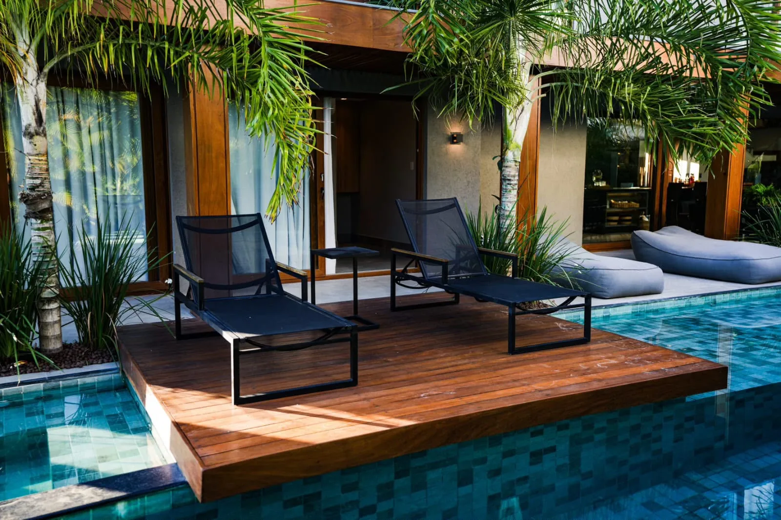 Deck da piscina ao sol, com espreguiçadeiras entre coqueiros